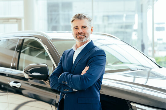 Aged beard man working at vehicle showroom. Portrait of a salesman in formal wear working at the dealership showing cars.