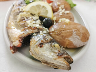 View of plated food, Healthy grilled mackerel dish stuffed with vegetable salad and potatoes, batata a murro, portuguese typical dish, regional cuisine, sliced tomato, lettuce, onion, olives and lemon