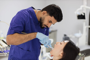 Fototapeta premium Happy patient and dentist concept. Young bearded asian male stomatologist treating teeth of a beautiful asian woman patient, using tooth drill. Oral health and hygiene.