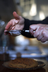 manos de repostera espolvoreando con colador una tarta con canela