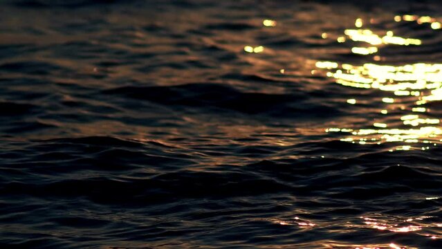 Sea, ocean surface with small waves and sunrise, sunset beams reflecting on the surface