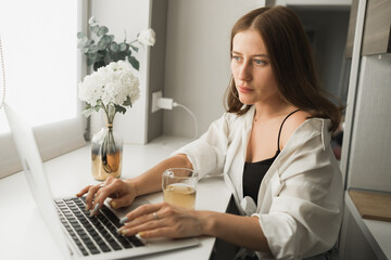 Close up of young pretty concentrated woman typing and browsing online on laptop working on computer while sitting in cozy room alone. Distance learning and work concept