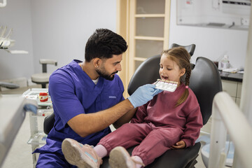 Tooth teeth tone palette. Stomatologist orthodontist male dentist choosing selecting color of patient cute little preschool girl teeth for whitening at clinic.
