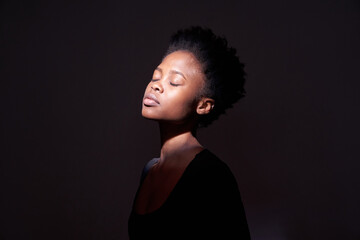 A black woman showing emotions. A woman with an emotional expression and closed eyes on a black background with a ray of light on her face. With space to copy. High quality photo