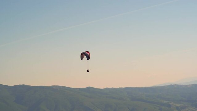 Single paraglider flying against the sunset pink sky above the mountain valley. Extreme sports - paragliding in the sky