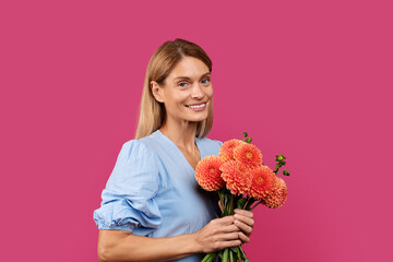 Portrait of happy adult caucasian female blonde in dress with bouquet of flowers looks at camera