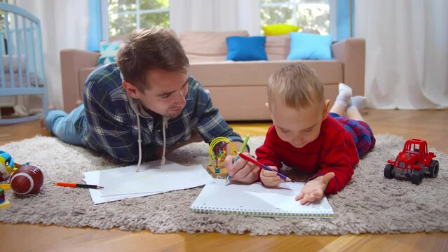 Loving dad and little son drawing with pencils lying on floor at home. Realtime
