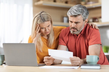 Anxious middle aged husband and wife checking correspondence, kitchen interior