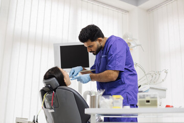 Beautiful smile with white teeth. Bearded male dentist treating teeth of a young asian woman using tooth drill and magnifying glass in the dental office.