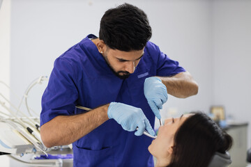 Happy patient and dentist concept. Young bearded asian male stomatologist treating teeth of a beautiful asian woman patient, using tooth drill. Oral health and hygiene.
