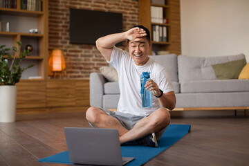 Happy tired asian man feeling exhausted after online workout, exercising with laptop computer,...
