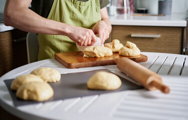 Unrecognizable male chef baker in green apron making dough balls. Cutting dough on a cutting board using spatula. Working at home kitchen concept, homemade baking. High quality image
