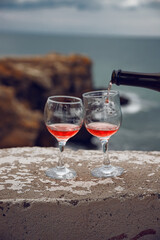 Two wine glasses on the background of the sea and mountains. Pink champagne. The drink is poured from the bottle into glasses.