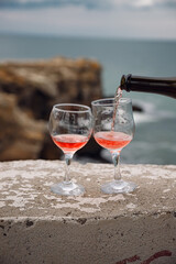 Two wine glasses on the background of the sea and mountains. Pink champagne. The drink is poured from the bottle into glasses.
