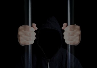 Anonymous criminal prisoner in hood holding prison bars on black background