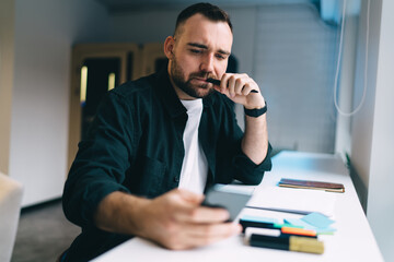 Obraz na płótnie Canvas Thoughtful man using smartphone during work