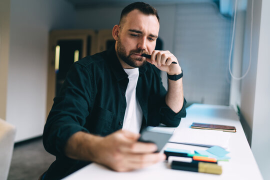 Thoughtful man using smartphone during work