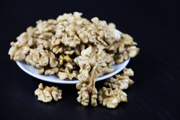 Peeled walnut kernels in a white plate on dark wooden table. Protein food for brain health