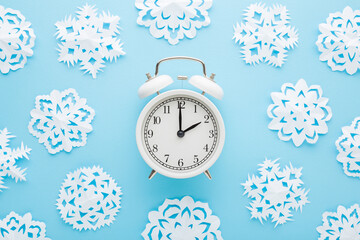 Different white snowflake shapes created from paper around alarm clock on light blue table...