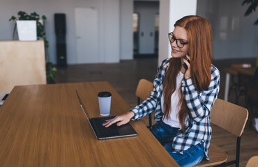 Young woman using laptop and talking on smartphone