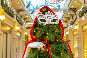 Christmas tree in a red cloak with a hood and an openwork masquerade mask in her hand.