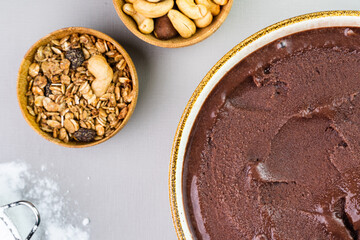 Brazilian açai in a white bowl, additional granola and nuts in small bamboo bowls. Cashew nuts and Pará. Top view. Grey background. Selective focus