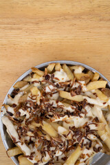 Fries. Top view of french fries with melted cheese and crispy onion, in a metal dish with a wooden background.