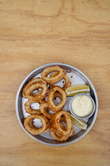 Seafood. Closeup view of fried squid rings with lemon and a dipping sauce in a metal dish on the wooden table.