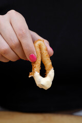 Eating seafood. Closeup view of a woman's holding a fried squid ring dipped in aioli sauce. 