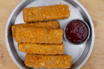 Gastronomy. Closeup view of fried mozzarella cheese fingers with a spicy dipping sauce, in a metal dish on the wooden table.