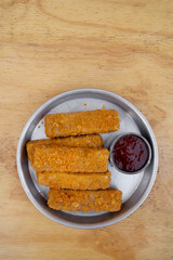Gastronomy. Top view of fried mozzarella cheese fingers with a spicy dipping sauce, in a metal dish on the wooden table.