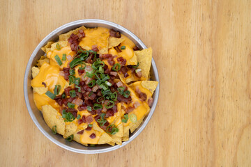 Nachos with cheddar background. Top view of nachos with cheddar cheese, green onion and crispy bacon in a metal dish on the wooden table.
