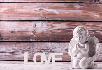 Little statue of white angle and word love  against brown textured wall. Selective focus. Place for text.