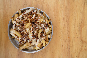 Fries. Top view of french fries with melted cheese and crispy onion, in a metal dish with a wooden background.