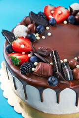 Birthday cake on blue background. Close up of cake decorated with fresh berries and chocolate sweets on color background. Delicious dessert for party