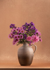 A lot of pink, lilac, autumn flowers in a light brown jug on an orange background. Variegated bouquet. Asters. Autumn still life. appeasement. Silence. Peace. Pleasure. Reflection. Card