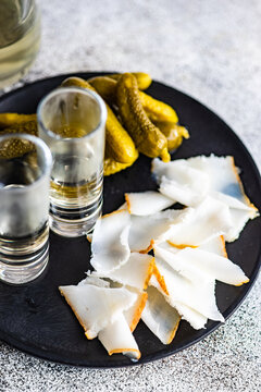 Overhead view of a plate of traditional Ukrainian cured pork fat (salo) with vodka shots and pickled gherkins