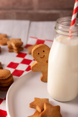 Homemade smiling gingerbread man cookie peeking out from behind a milk glass jar. These cookies are traditionally made in the holiday season for Christmas.