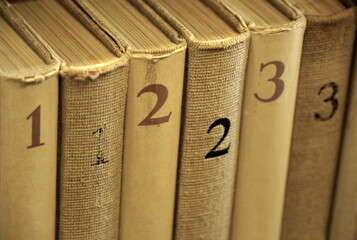 Old worn books in three volumes on a bookshelf in sepia color
