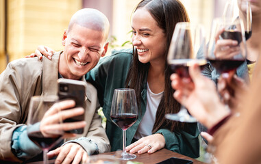 Young friends having fun drinking red wine at trendy winery bar - Happy people sharing content on mobile phone together at open air restaurant garden - Youth life style concept on bright warm filter