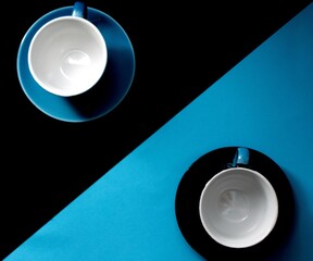 Blue cup on a black background, black cup on a blue background divided diagonally. Coffee together concept. Tea for a couple in love. Creative photography, top view.