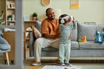 Full length portrait of cute black child wearing VR headset and enjoying virtual reality entertainment for children, copy space