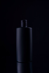 black shampoo bottle on black background still life