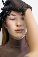 Red-haired girl with freckles in a beauty salon paints her eyebrows. The eyebrow master draws a...