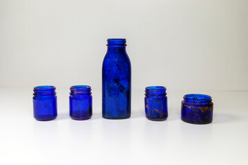 Aged and patina vintage blue glass medical bottles on a white and gray background with copyspace.