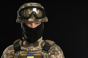 Soldier in Ukrainian military uniform, tactical goggles and balaclava on black background. Space...