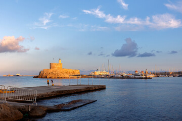 Obraz premium Colorful panoramic view of Agios Nikolaos fortress with yachts in Mandraki port at sunset, Rhodes Greece. High quality photo