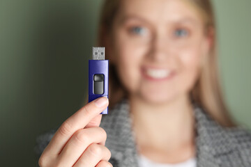 Woman holding usb flash drive against green background, focus on hand