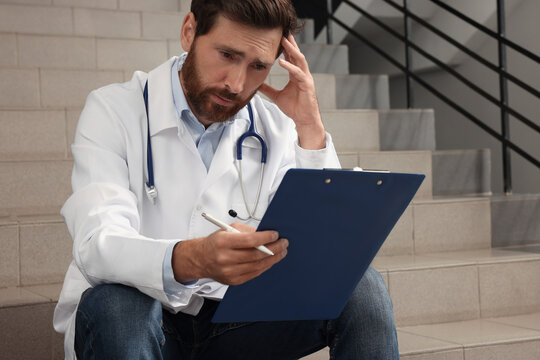 Upset doctor with clipboard sitting on stairs in hospital