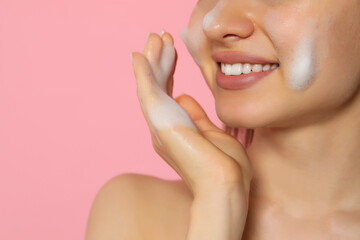 Obraz na płótnie Canvas Young woman washing face with cleansing foam on pink background, closeup and space for text. Skin care cosmetic